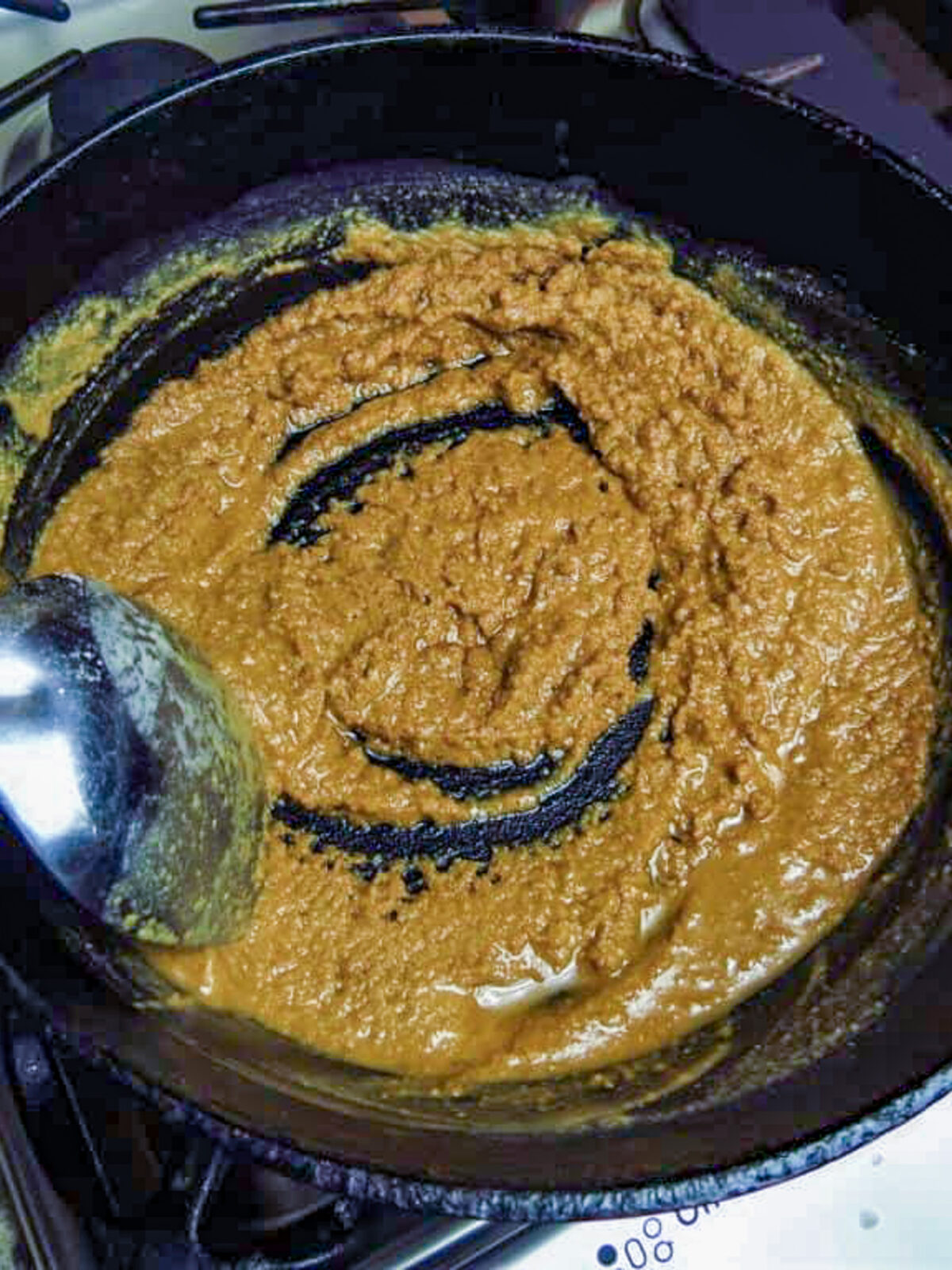 A silver spoon stirring a light colored roux in a black pot.