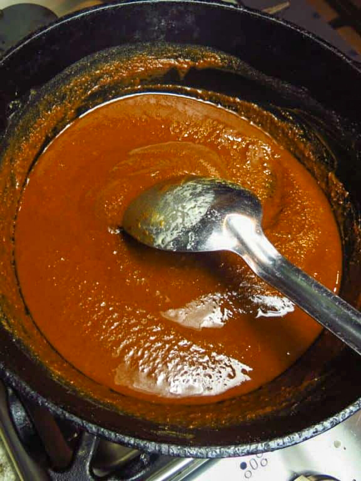 A black pot of dark roux with a long-handled silver spoon in the center.