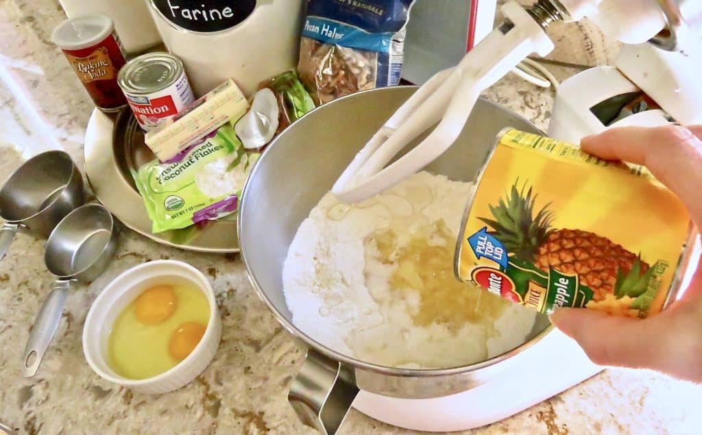 A can of pineapple poured into a bowl of ingredients on a stand mixer.