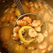 Shrimp and lemon slice spooned over a boiling pot.