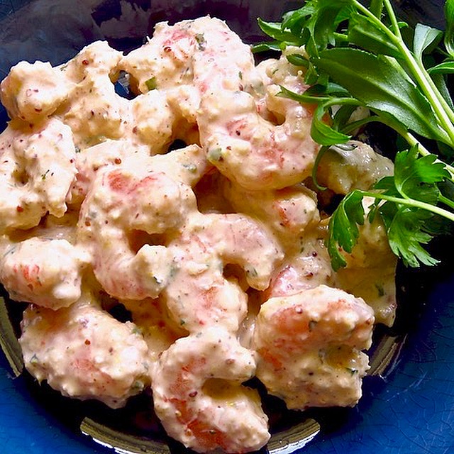 Shrimp covered with remoulade sauce in a blue bowl .