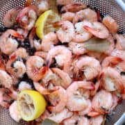 A pan of boiled shrimp with lemons, bay leaves, and seasonings.