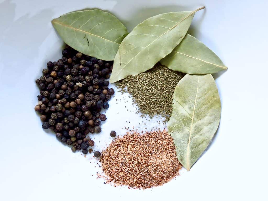 Peppercorns, bay leaves, salt, and other seasonings in a white bowl.