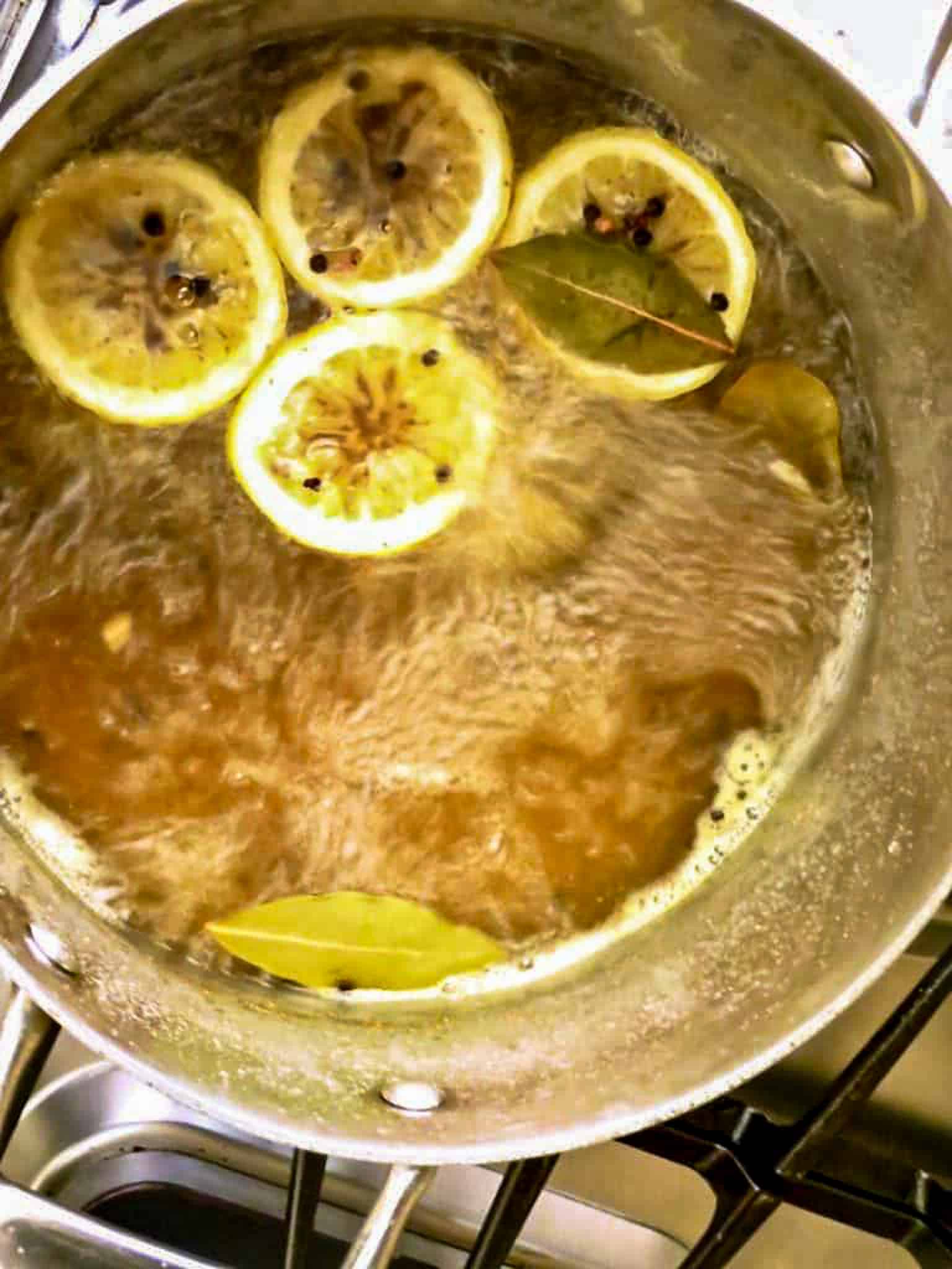 A pot of boiling water with lemon halves and bay leaves.