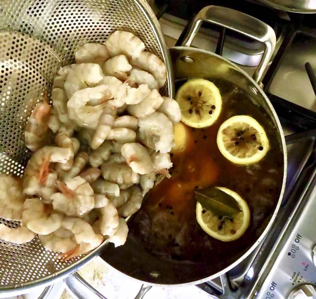 Fresh shrimp poured into a pot of boiling water with lemon halves and seasonings.