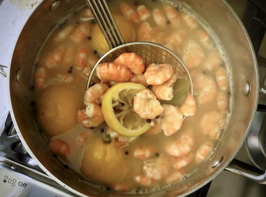 Pot of shrimp boiling with lemon halves in a strainer.