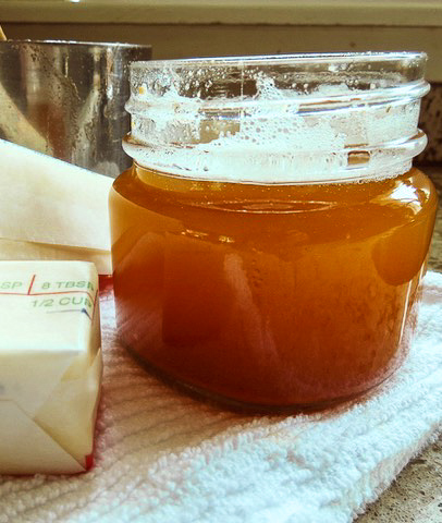 A glass jar of brown butter with a stick of butter.