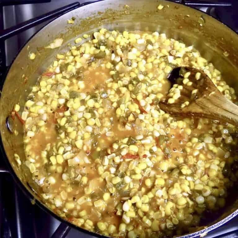 Stirring a pan of corn macque choux with a wooden spoon.