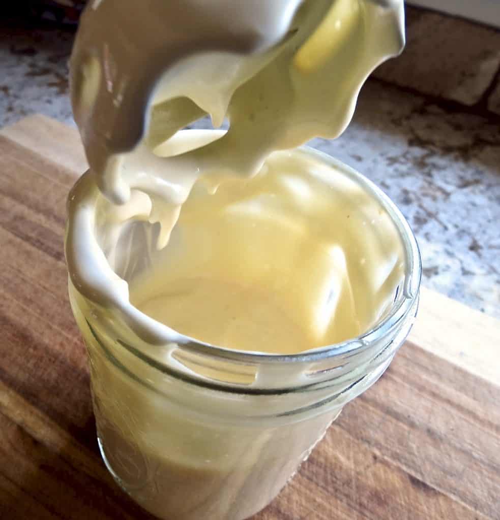 A mason jar of mayonnaise with the end of an immersion blender coming out of it dripping with mayo.