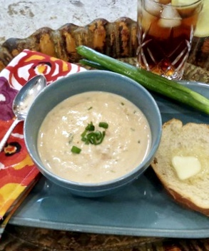 Bowl of seafood bisque garnished with sliced green onion and buttered bread.