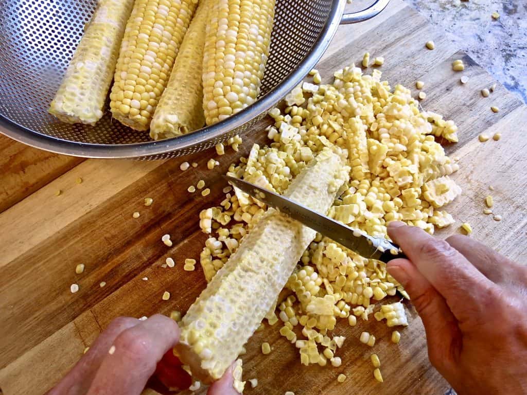 Cutting fresh corn from cob on wooden cutting board
