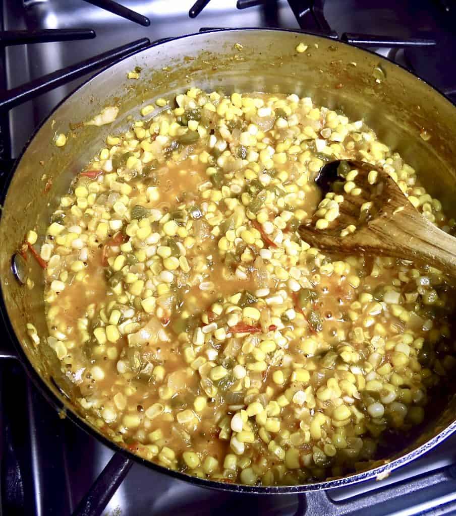 Stirring a pan of corn macque choux with a wooden spoon.