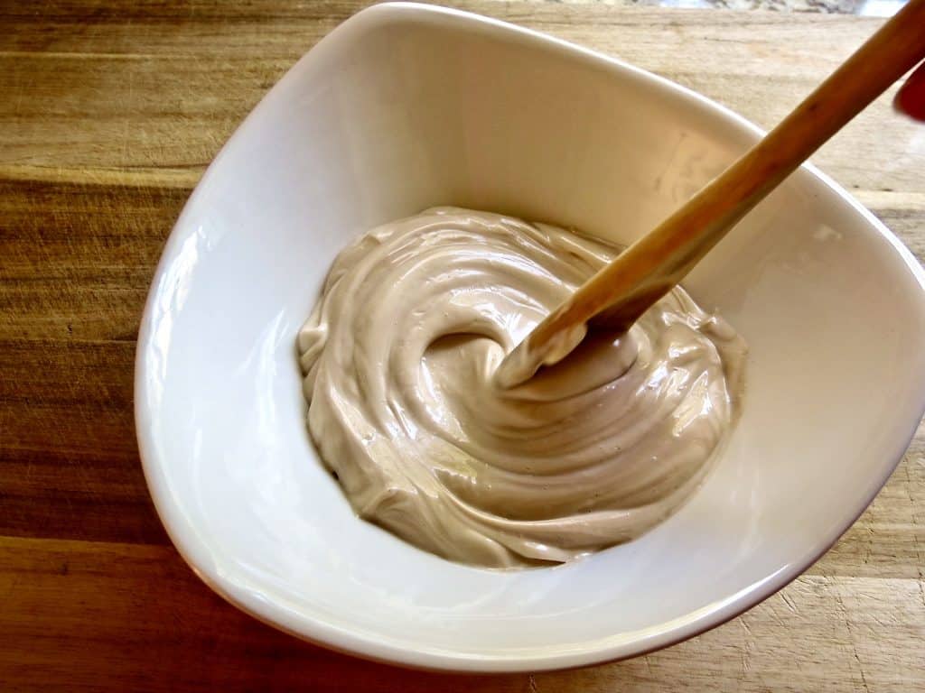wooden spoon mixing salad dressing in white bowl for