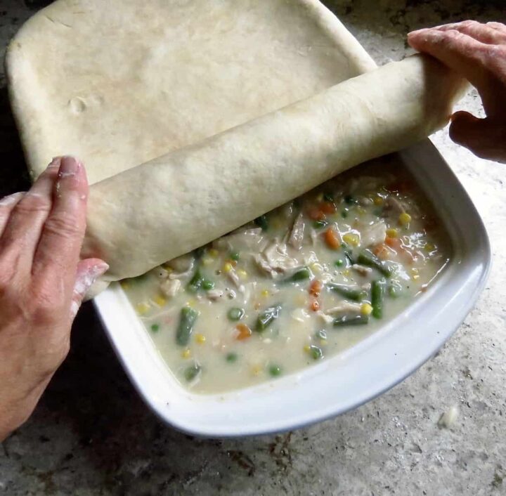 Rolling pie dough onto Chicken Pot Pie.