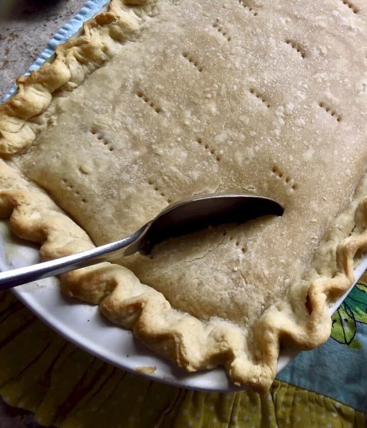 Spoon dipping into crust of baked chicken pot pie .