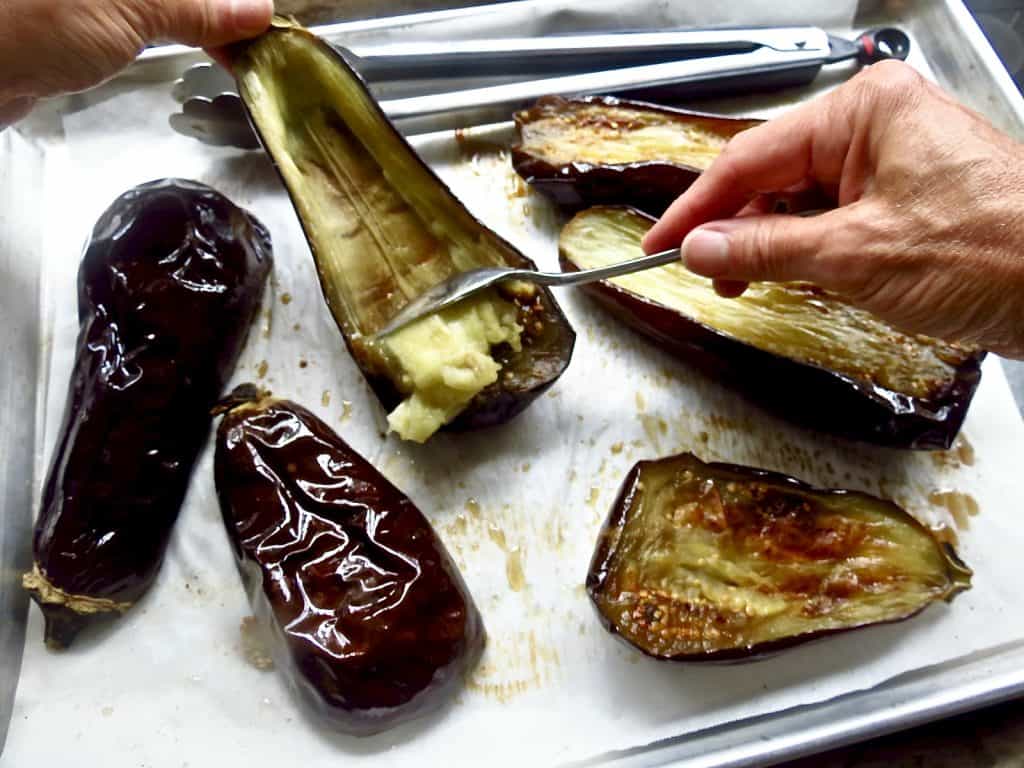 Scooping out eggplant from roasted purple shells with a spoon.