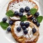 French toast with powdered sugar and blue berries on a white plate.