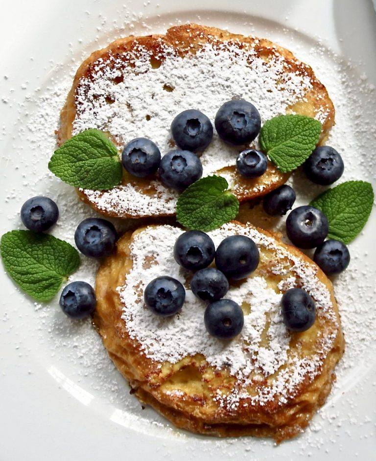 French toast with powdered sugar and blue berries on a white plate.