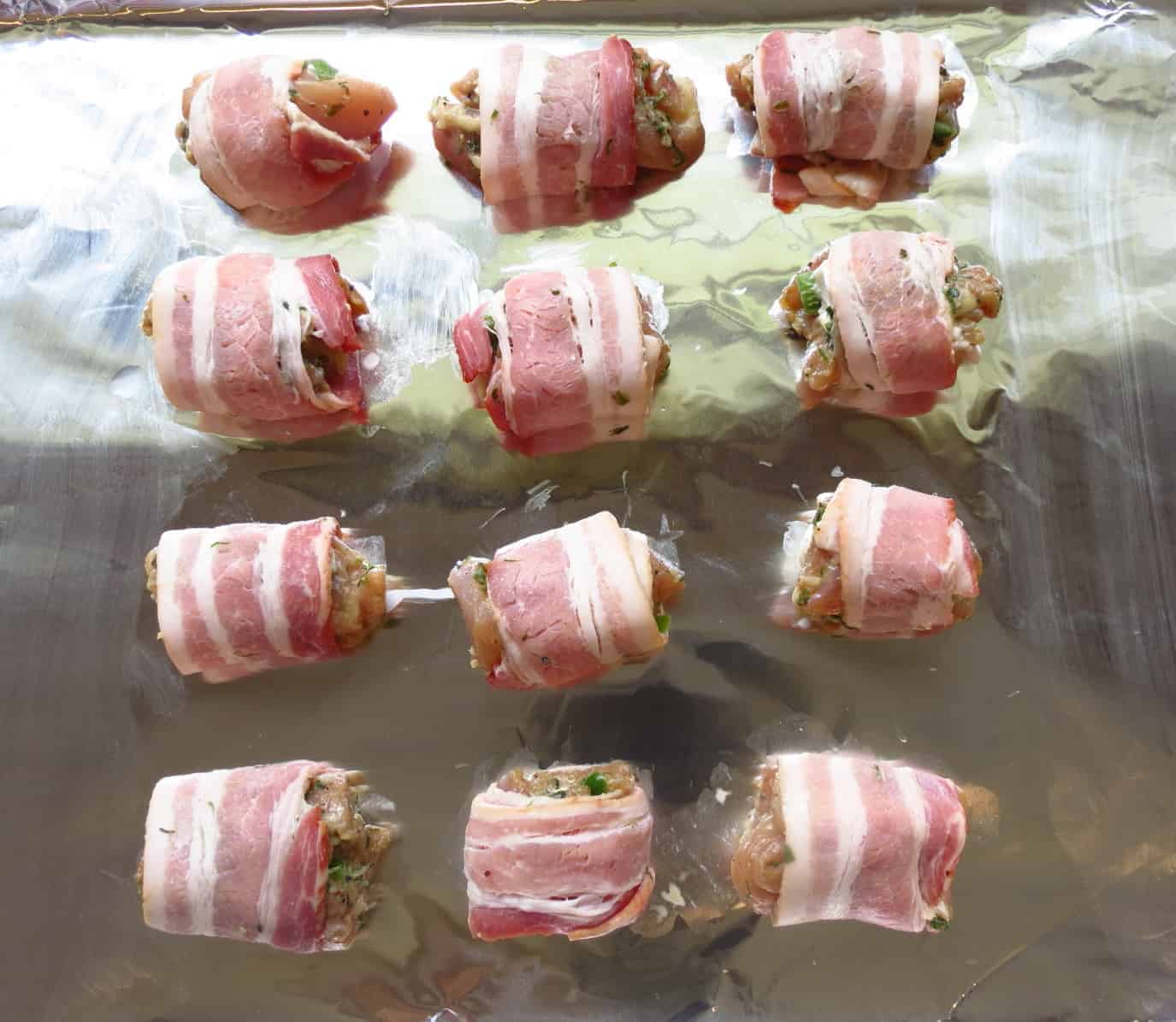 Stuffed Chicken Wrapped In Bacon ready for oven lined up on a foil wrapped cookie sheet.