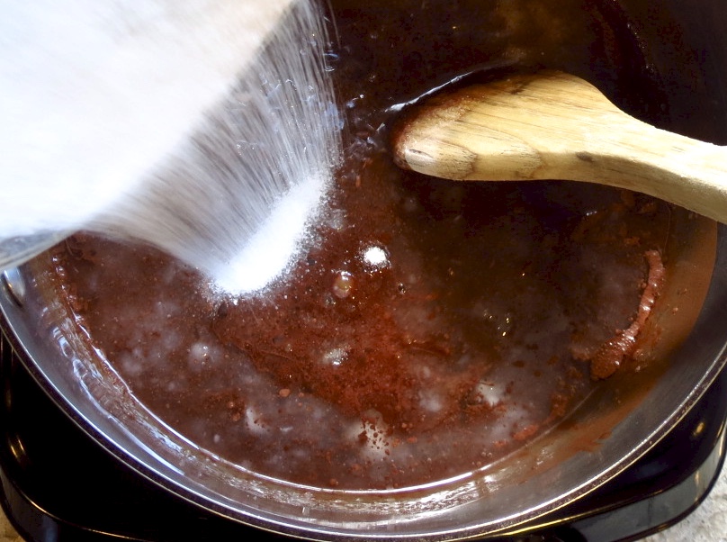 Adding sugar to chocolate in a pot.