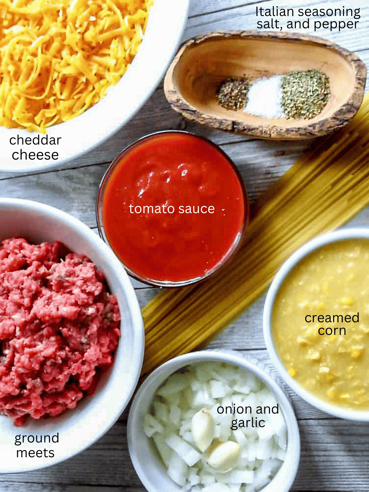 Ingredients for a pasta dish with ground meat, onions, tomato sauce, corn, seasoning, and cheese.