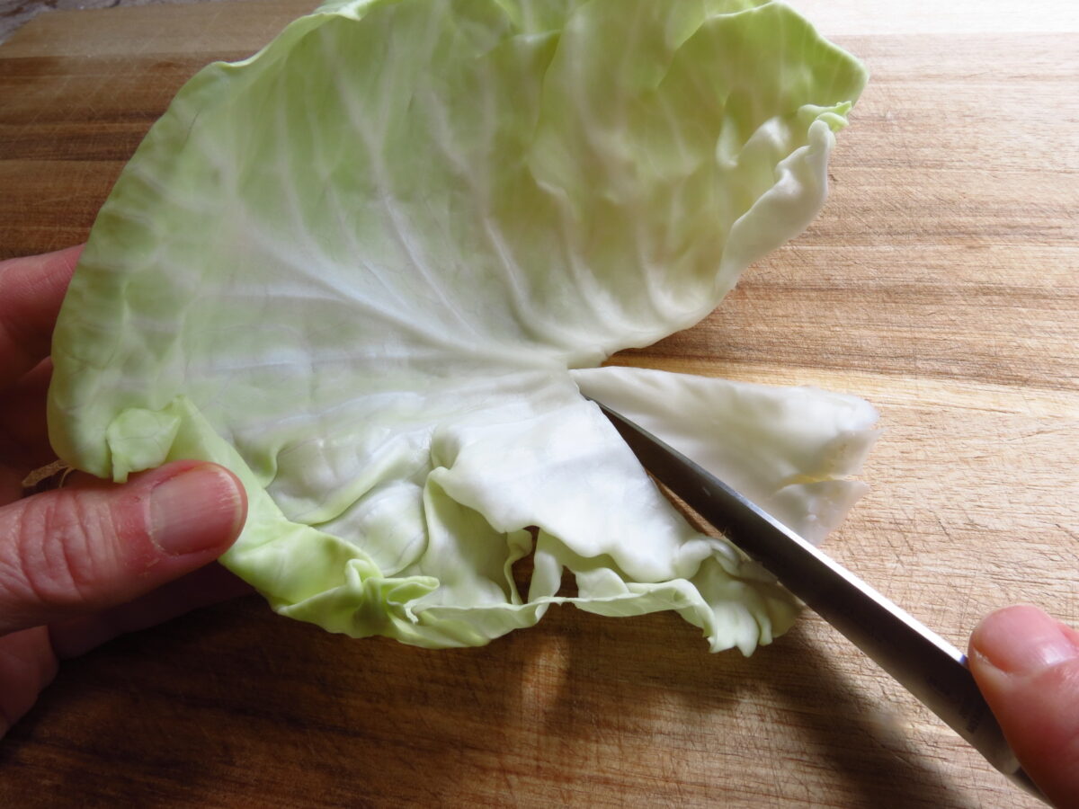 Raw cabbage leaves being cut into on cutting board for Classic Cabbage rolls.