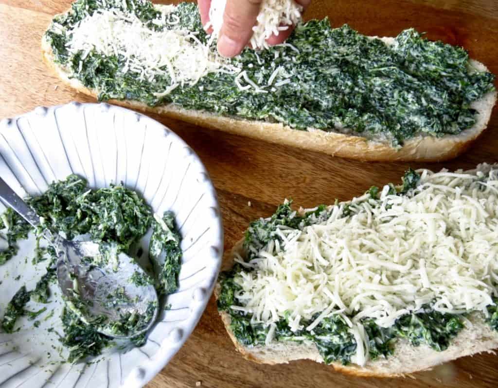 Two loaves of French Bread spread with spinach mix from a bowl of spinach mix and topped with white cheese on bread.