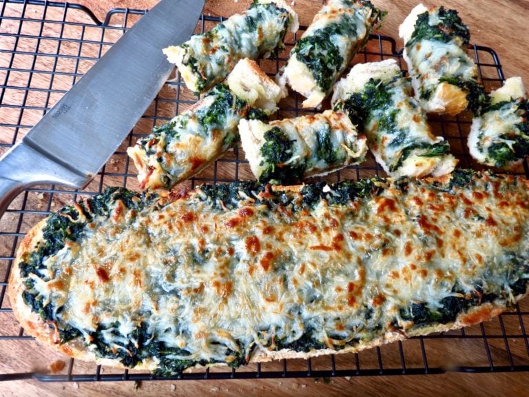 Loaf of spinach bread and cut up pieces on a rack with a knife.