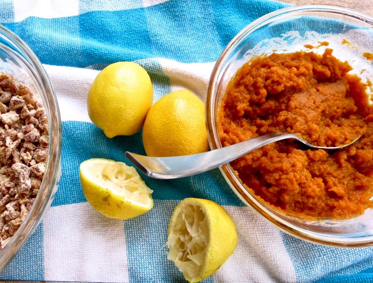 A glass bowl besides cut and whole lemons with a bowl of dates sitting on a blue and white dishtowel.