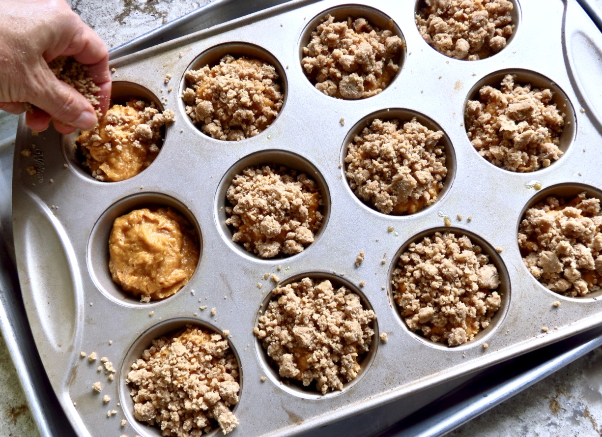  Pumpkin Muffins With Streusel  in a muffin tbaking dish with streusel being added on top.