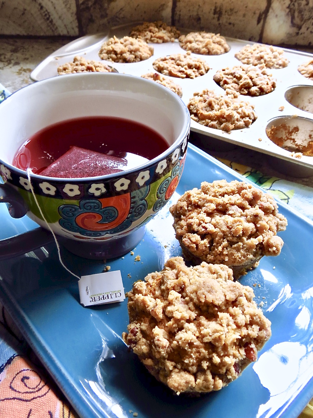 Two Pumpkin Muffins With Streusel on a blue plate with a multi-colored cup.