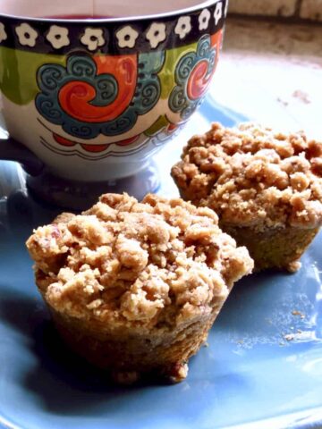 Two Pumpkin Streusel Muffins on a blue plate with a multi-colored cup.