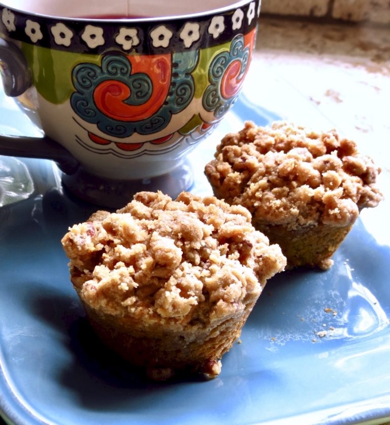 Two Pumpkin Streusel Muffins on a blue plate with a multi-colored cup.