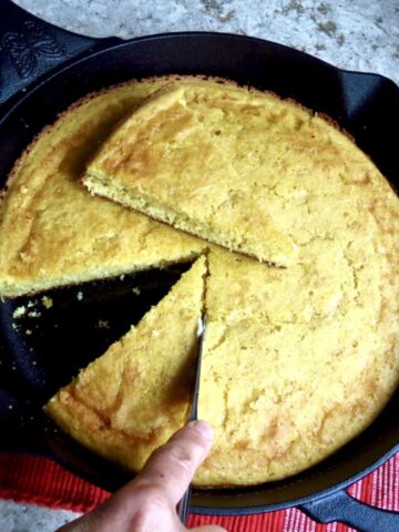 Iron Skillet Cornbread in black iron skillet with slices of bread being cut out of it.