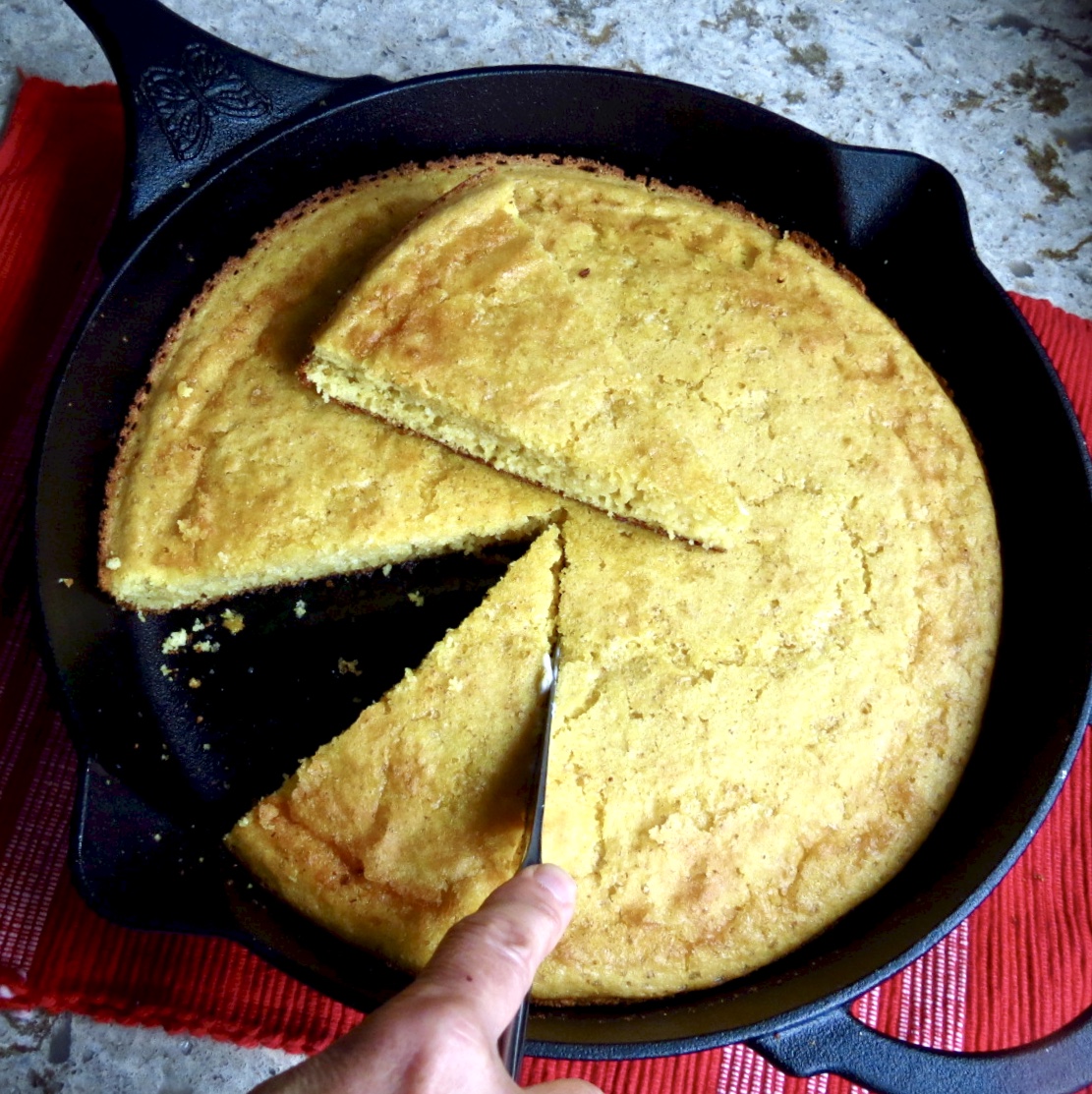 Iron Skillet Cornbread in black iron skillet with slices of bread being cut out of it.