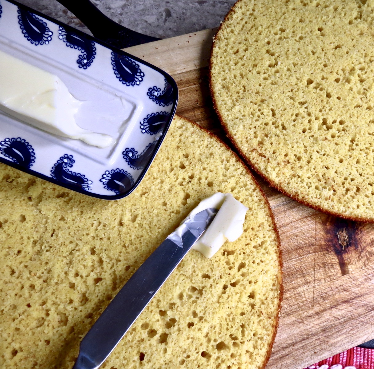 Iron Skillet Cornbread Sliced in half with butter being slathered on it near butter dish.