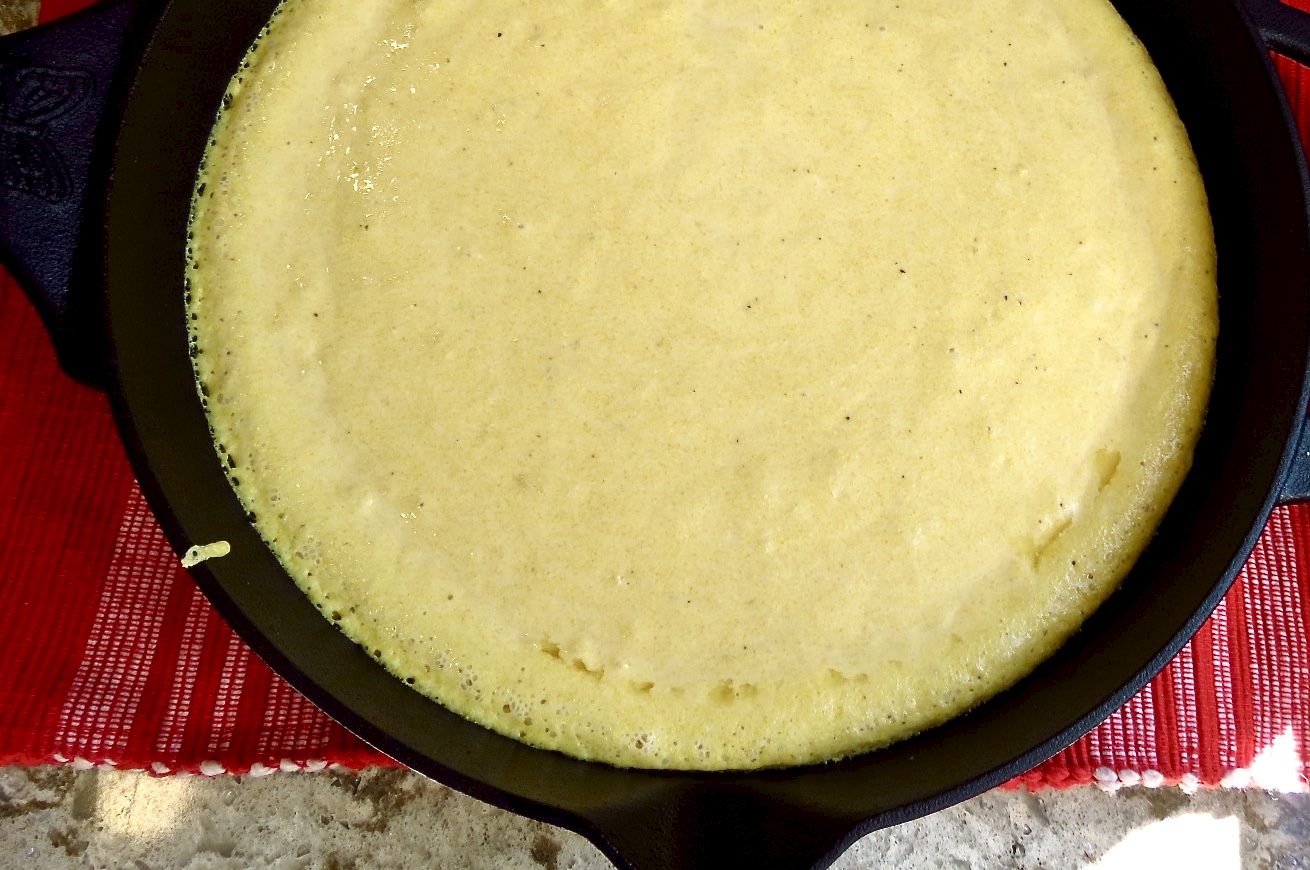 Iron Skillet Cornbread batter after it is poured into hot black iron skillet with bubbly edges.