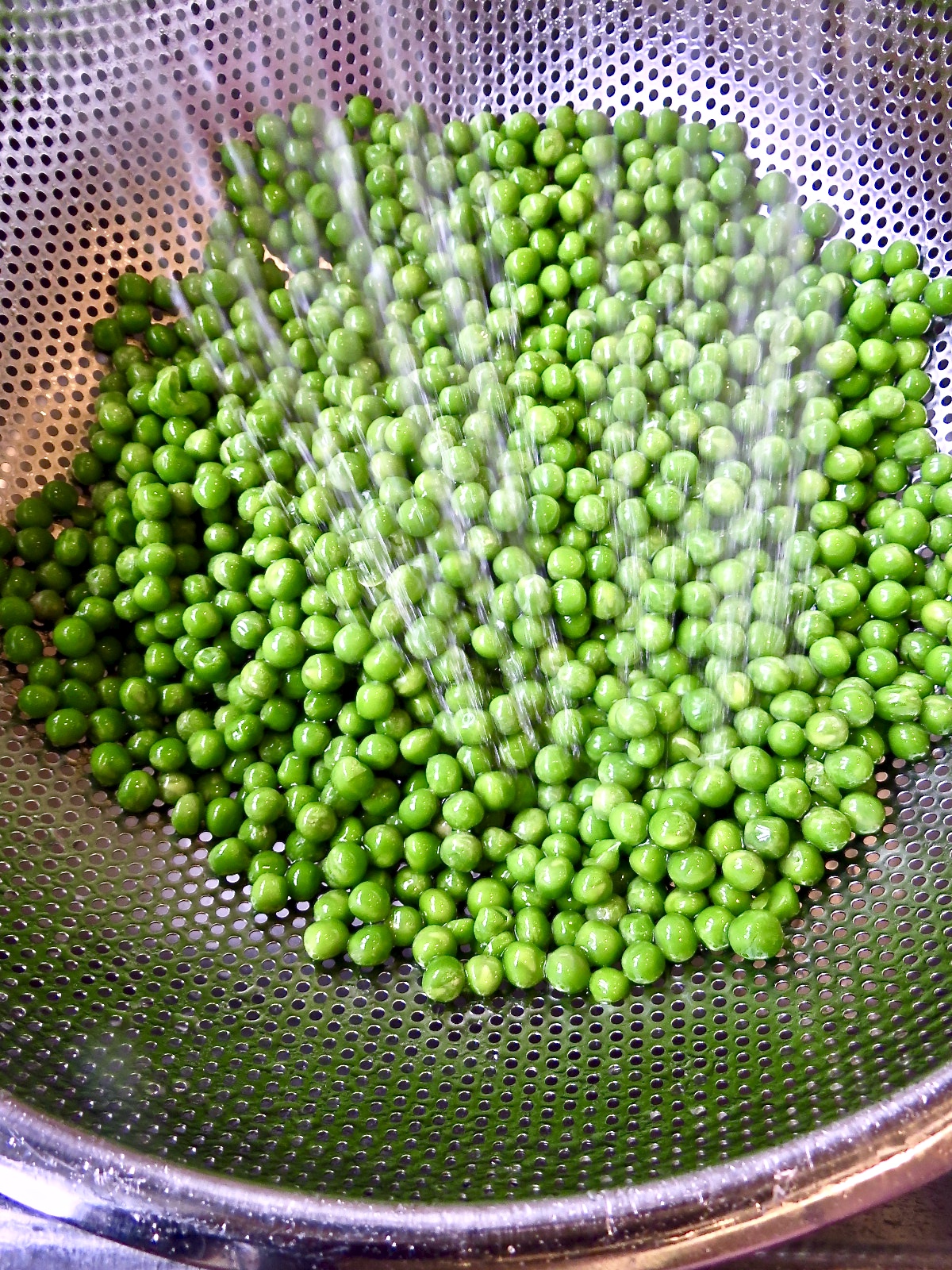 Green Peas being rinsed in a silver colander for Pea Salad, The Forgotten Side Dish.