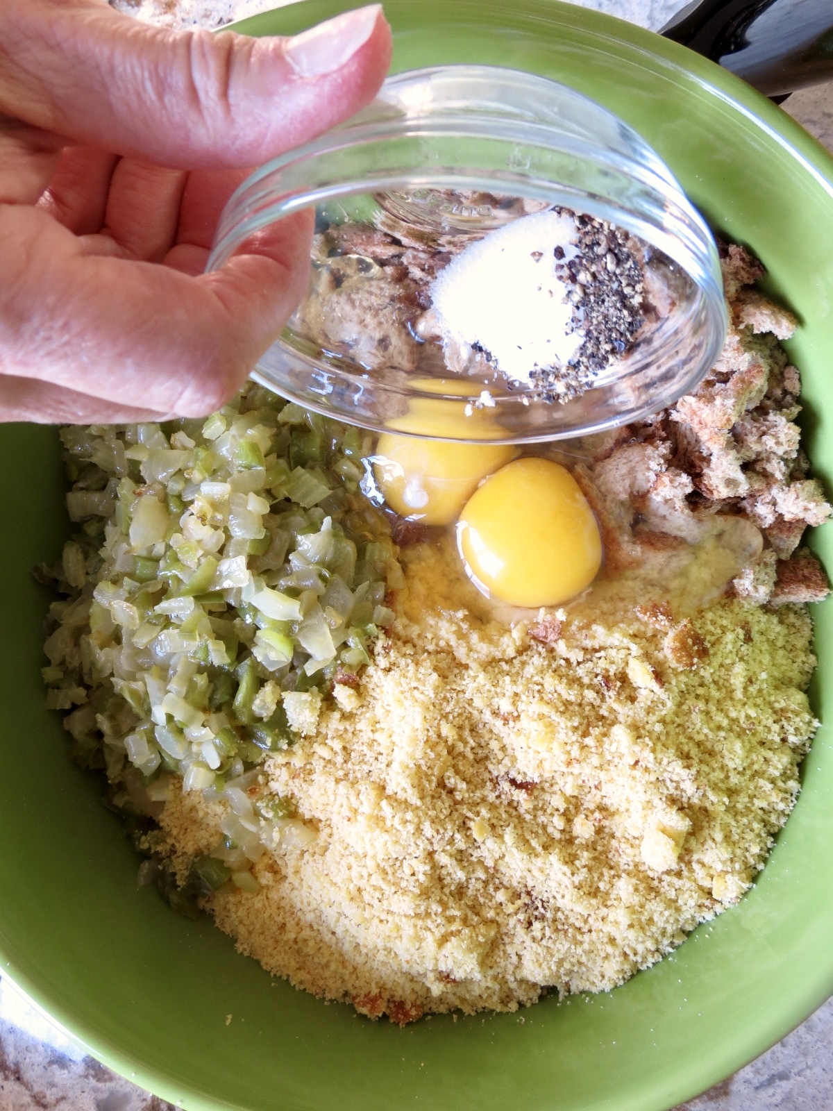 Cornbread, bread crumbs, eggs and vegetables in a green bowl with seasonings to make Cornbread Dressing.