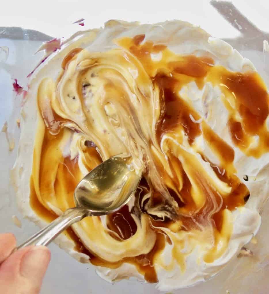 Spooning caramel sauce on top of layer of whipped cream.