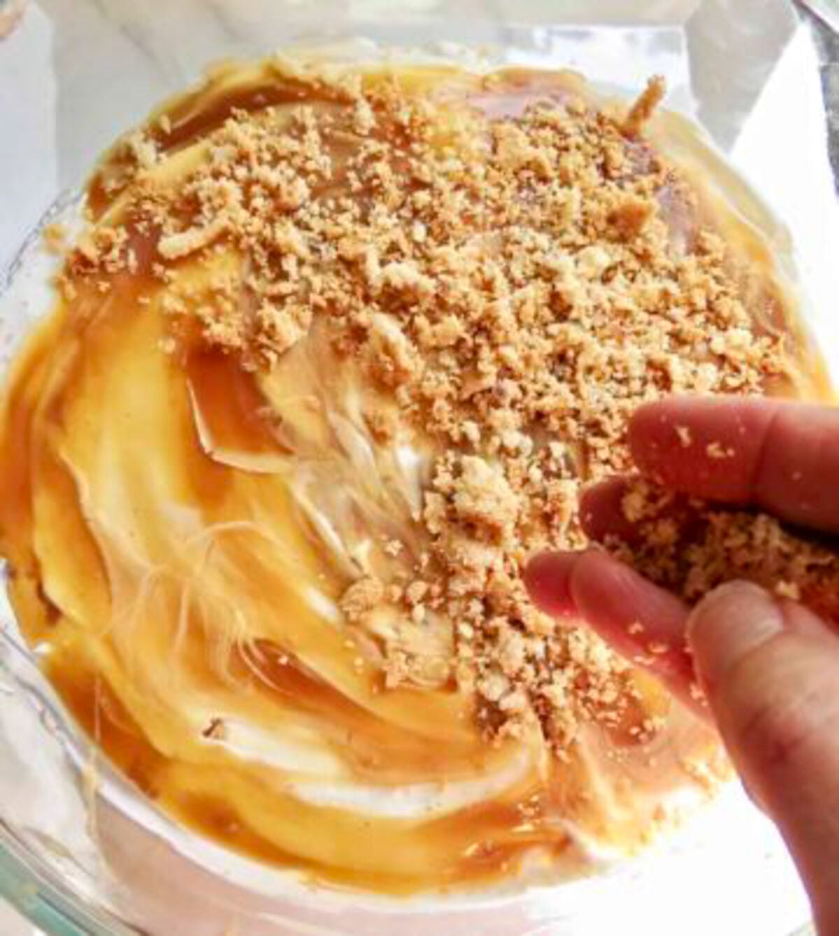 Two fingers sprinkling crumbs over a cram and caramel topping.