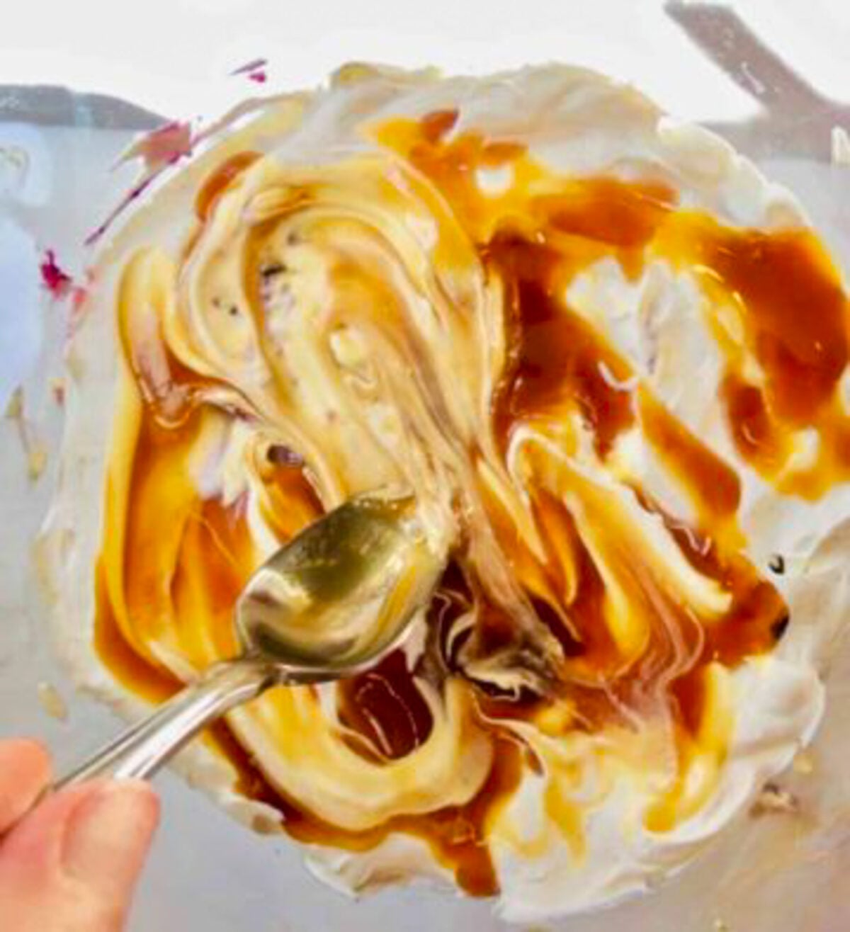 A spoon spreading caramel syrup over a creamy topping.