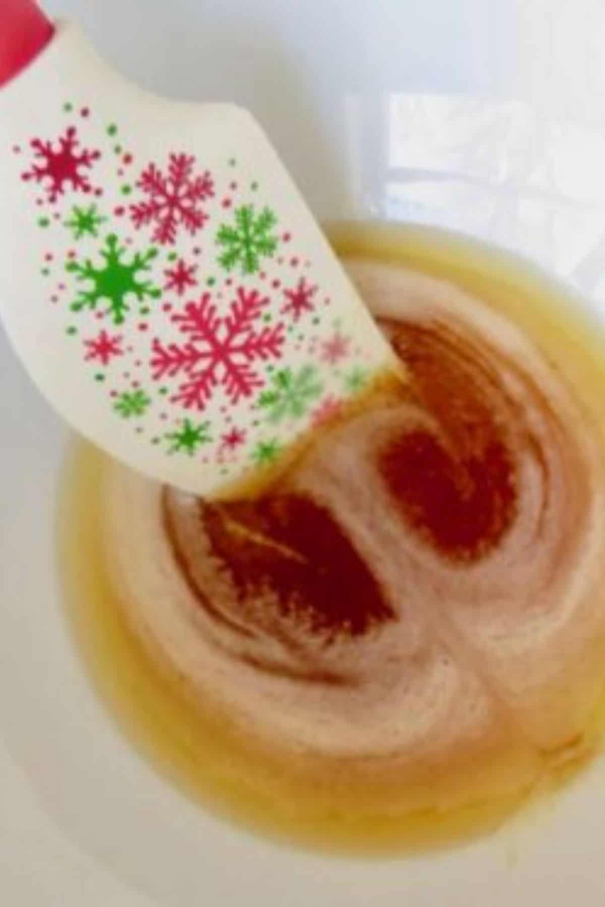 A Christmas spatula stirring browned butter in a white bowl.