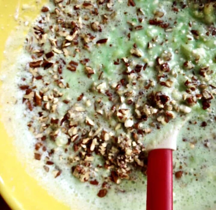 Red spatula stirring pecans into mixture of lime yellow and cream cheese, pineapple mixture for Congealed Salad, Cherry Or Lime Flavored.