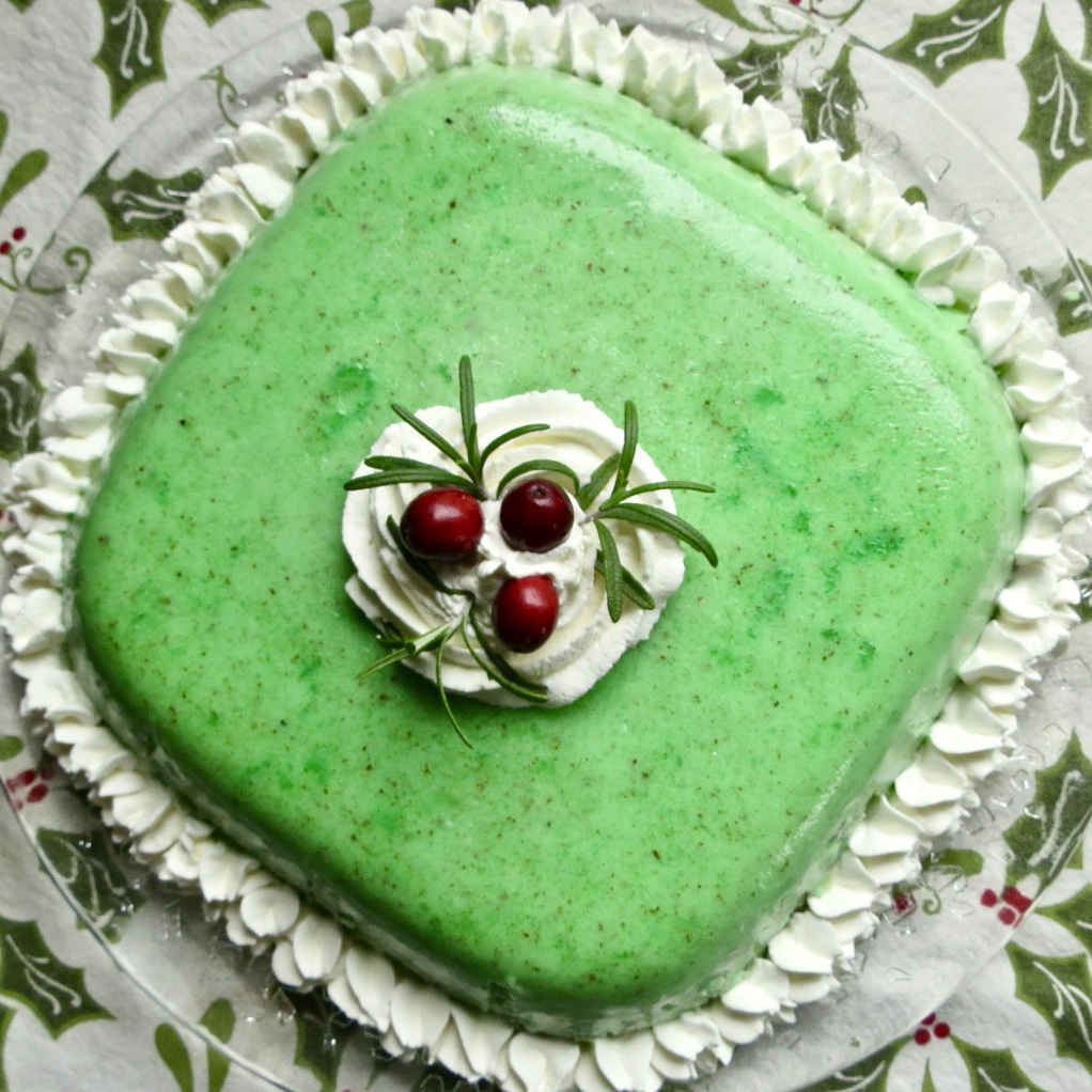 A swear mold of green congealed salad with whipped cream piping around and on top with red cranberries and green rosemary for garnish for Congealed Salad, Cherry Or Lime Flavored.
