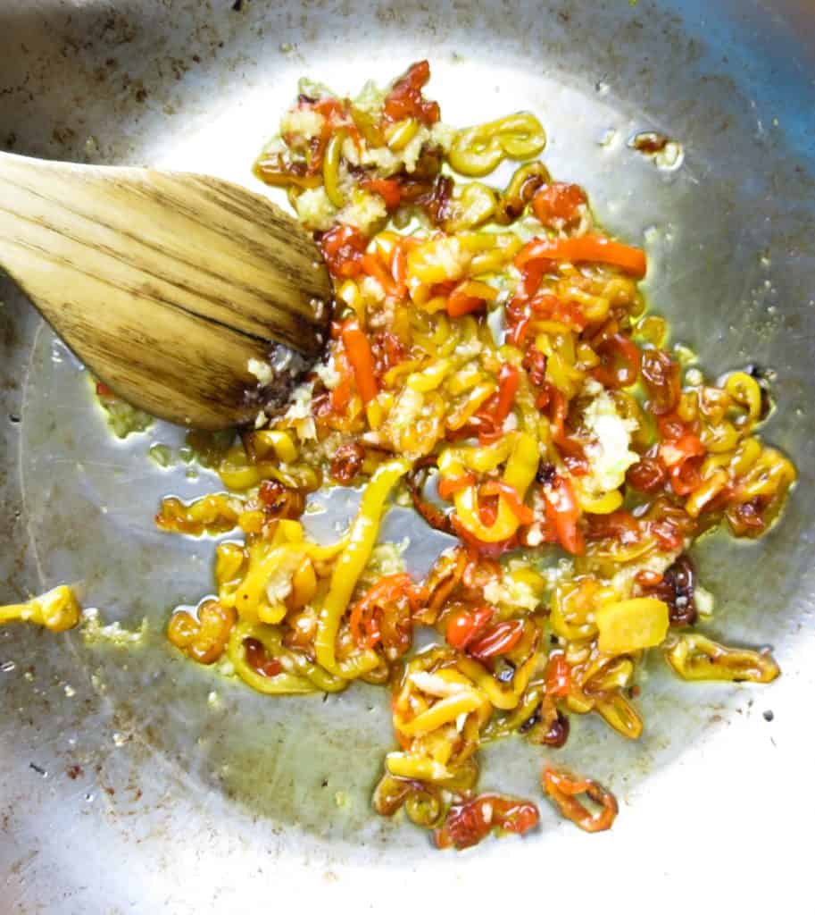 Sautéed sweet peppers in a pan with a wooden spoon.