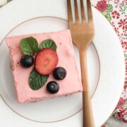 A white plate with a gold fork and a piece of Keto Strawberry Jello Dessert on it and berries on top.