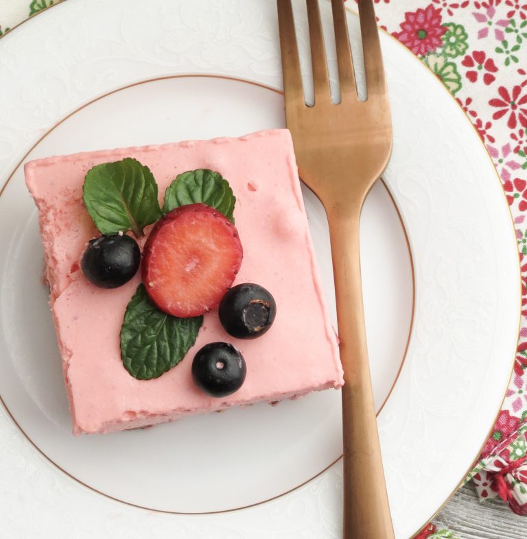 A white plate with a gold fork and a piece of Keto Strawberry Jello Dessert on it and berries on top.