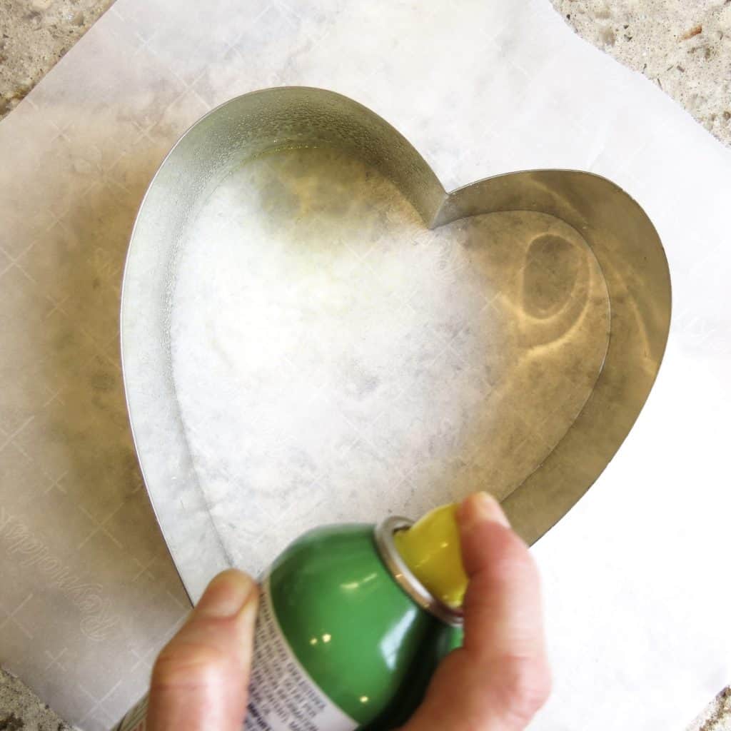 Spraying vegetable spray in a heart shaped tin mold.