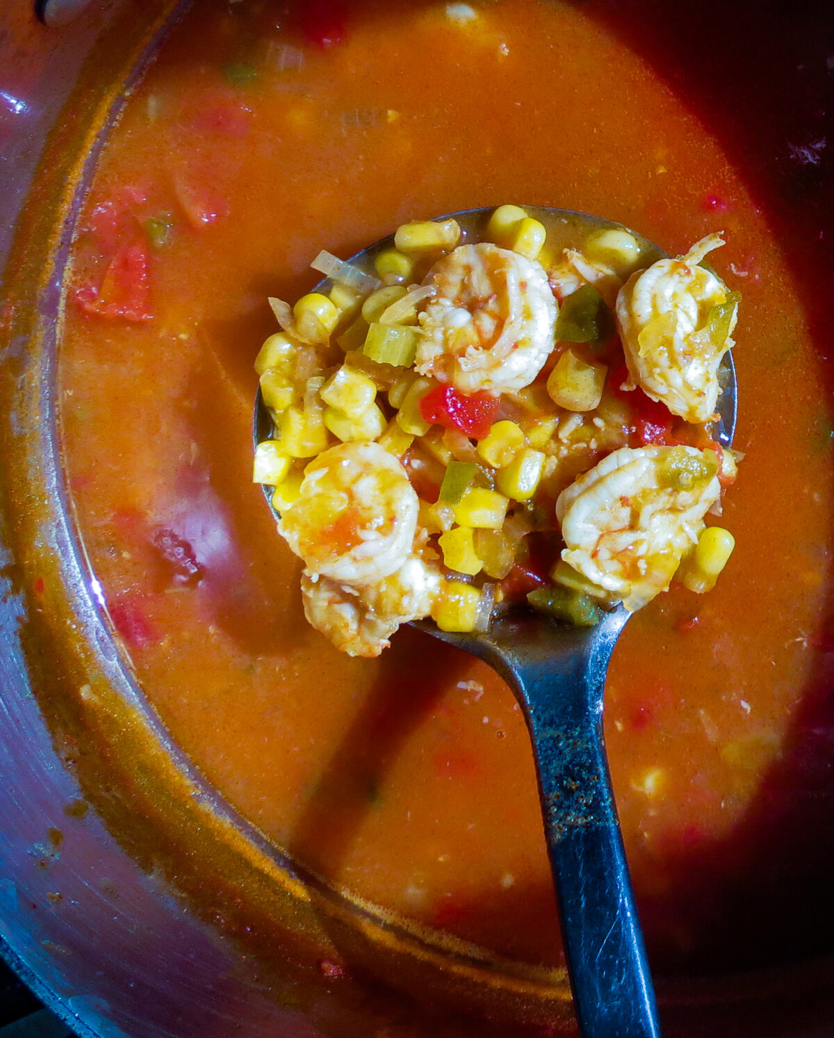 A pot of Shrimp And Corn Soup with a ladle stirring soup.